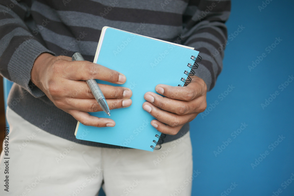 man hand holding a blue color notepad with pen man hand holding a blue color notepad with pen