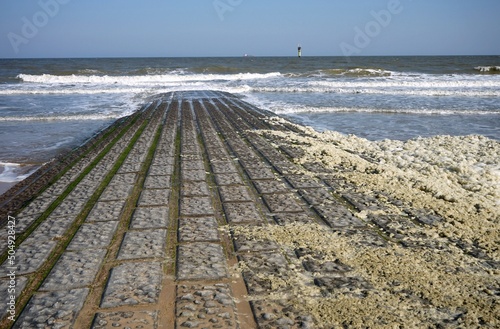 Brandung mit weißem und gelbem Schaum am Strand der Nordsee mit Wellenbrecher als Küstenschutz bei blauem Himmel und Sonnenschein in Knokke-Heist bei Brügge in Westflandern in Belgien photo