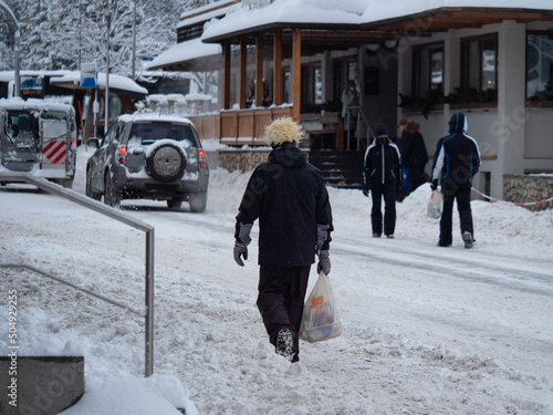 Skiers in ski Suits Walking down a Snow-filled Street with Shopping Bags in teir Hands photo