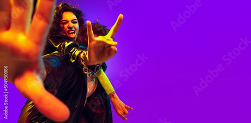 Close-up hands of young couple of rock-and-roll musicians wearing black leather outfits gesturing, shouting on blue yellow background in neon light. Flyer