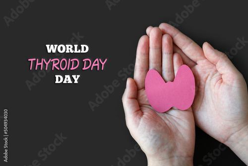 World Thyroid Day. Adult hands hold paper form of the thyroid gland on black background. Problems with thyroid. Polycystic disease.