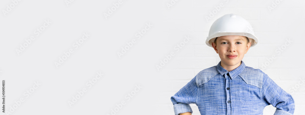 Smiling boy with white helmet cup on his head. Child dreams of being an engineer, architect or builder worker. Construction, renovation, choice of profession, education. Banner background, copy space.