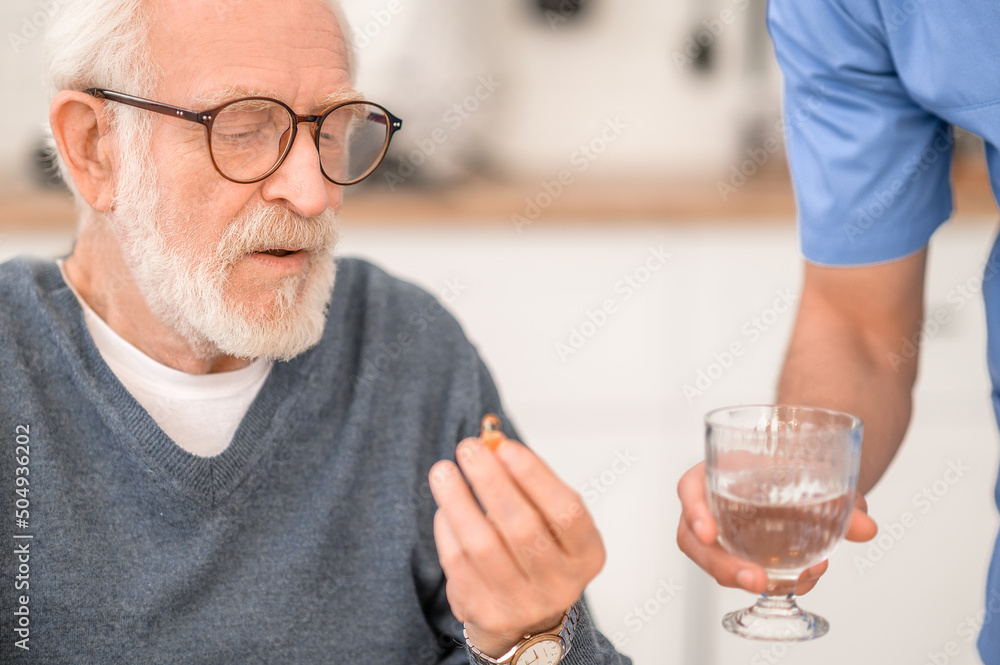 Pensioner taking a pill with water supervised by his caregiver Pensioner taking a pill with water supervised by his caregiver
