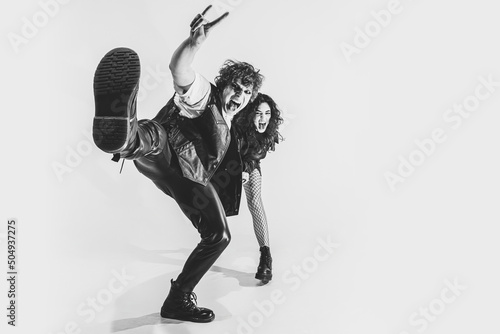Wide angle view. Monochrome portrait of crazy musicians, young boy and girl wearing black leather outfits moving on white studio background. Music, youth photo