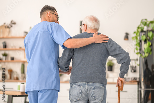 фотографія Medical worker assisting his patient to walk with a cane