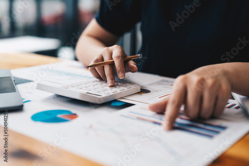 Close up of business woman or accountant hand holding pen working on calculator to calculate business data, accountancy document and laptop computer at office, business concept