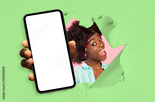 canvas print motiv - Prostock-studio : Happy excited young african american female with open mouth looks through hole in green paper and shows smartphone