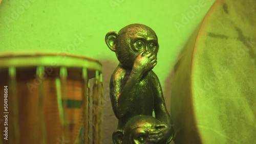 Golden monkey in green light next to drums covering her mouth and eyes of another monkey mysterious suspense slow motion photo