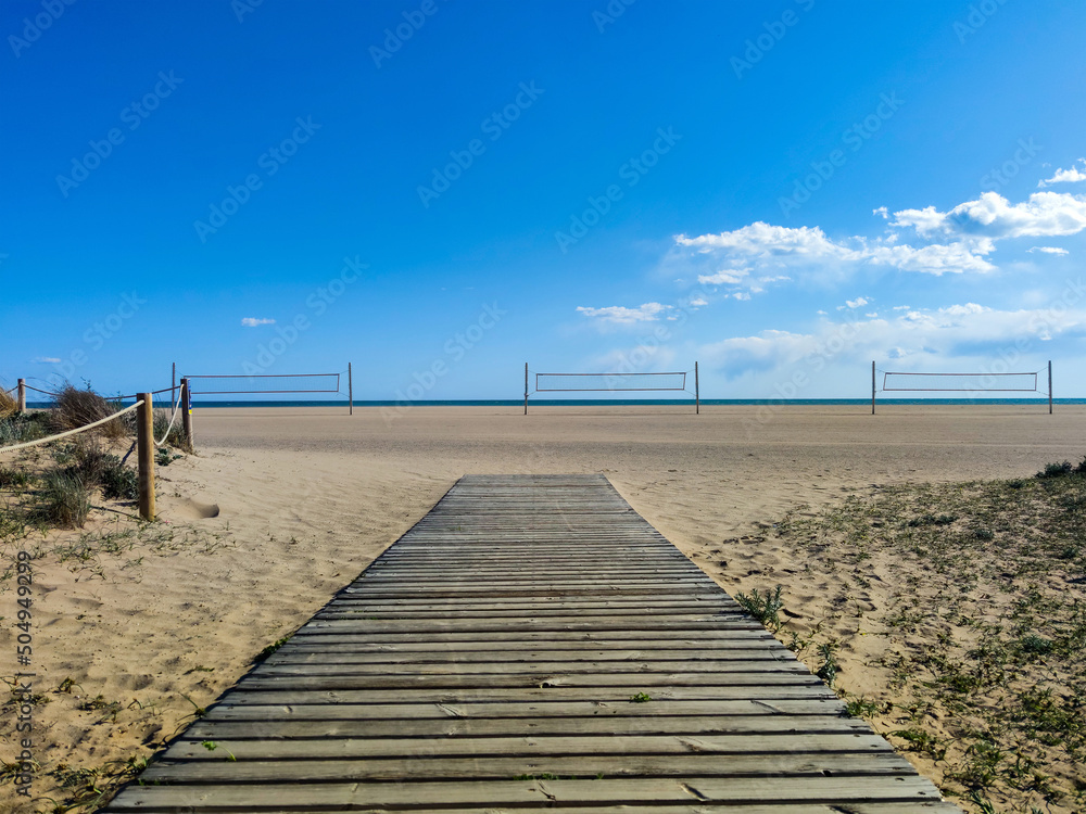 wooden fence and path with volleyball nets on sandy beach with blue ocean view on horizon
