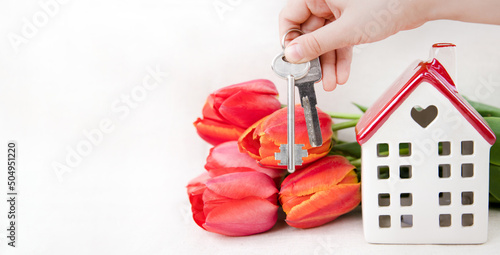 A white house with a red roof, apartment keys and tulips on a white background.The theme of love and celebration.The concept of delivery, home purchase and mortgage.