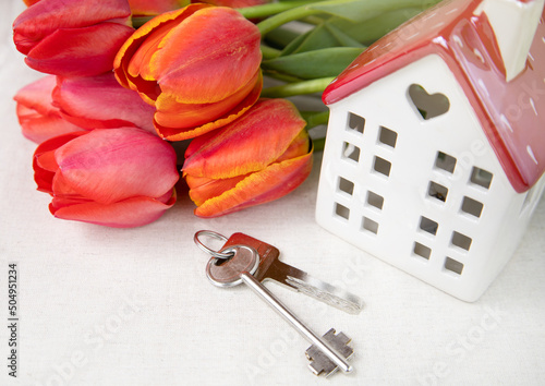 A white house with a red roof, apartment keys and tulips on a white background.The theme of love and celebration.The concept of delivery, home purchase and mortgage.