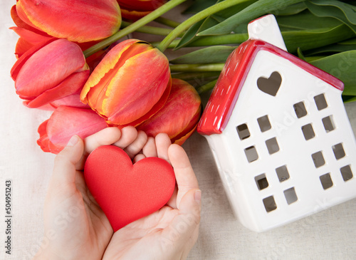 Red tulips, a house and a heart in the hands of a child. The concept of love, family and mental health