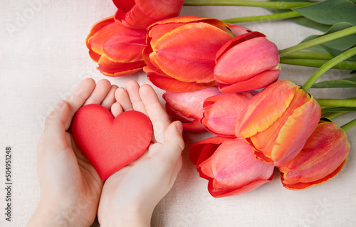 Red tulips and a heart in the hands of a child. The concept of love, family and mental health