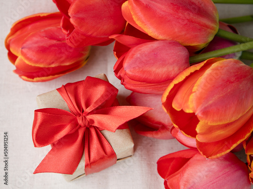 A gift and red tulips on a light background.The concept of love, care and celebration. Birthday or Valentine's Day