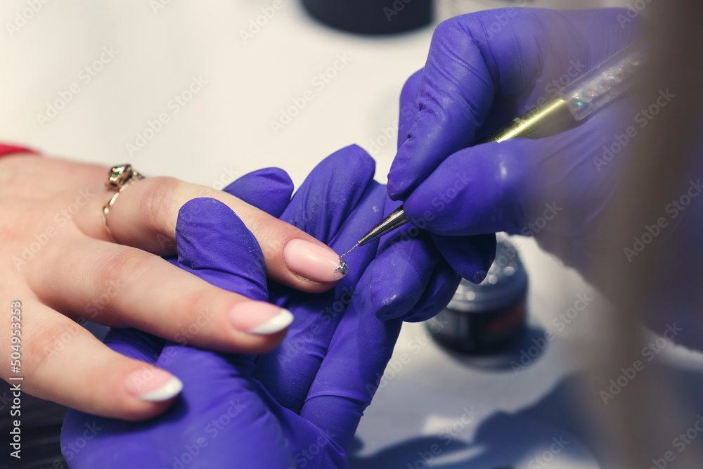 a manicurist makes a manicure to a client, applies a second coat of varnish with silver glitter a manicurist makes a manicure to a client, applies a second coat of varnish with silver glitter