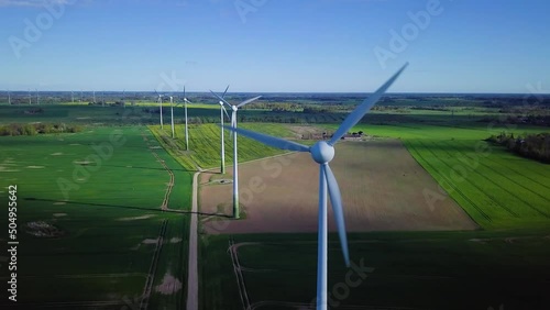 Aerial view of wind turbines generating renewable energy in the wind farm, sunny spring day, low flyover over green agricultural cereal fields, countryside roads, drone dolly shot moving right photo