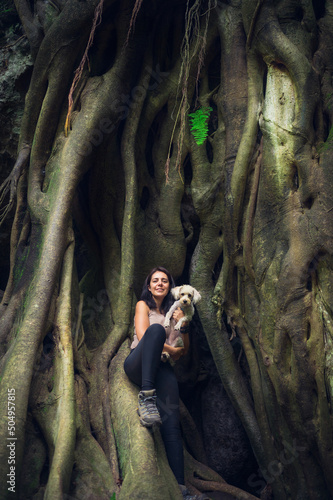 Young woman posing with her cub on giant root tree in tropical forest. Woman and pet in green wet forest on sunny day. Sustainable tourism concept. Amatlan, Mexico photo