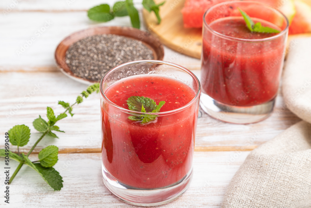 Watermelon juice with chia seeds and mint in glass on a white wooden background with linen textile. Side view. Watermelon juice with chia seeds and mint in glass on a white wooden background with linen textile. Side view.