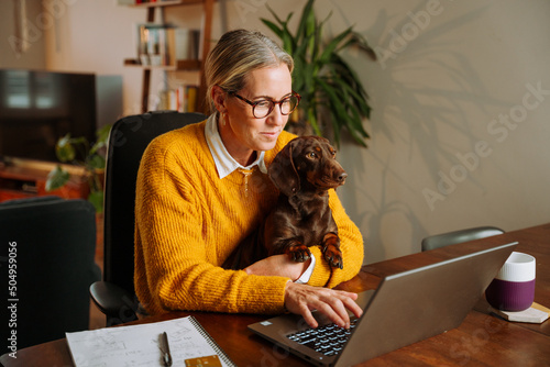 Caucasian female business woman working from home holding pet dog on her lap photo