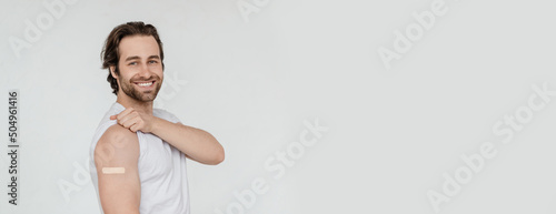 Glad millennial caucasian guy with stubble shows shoulder with band-aid isolated on white background