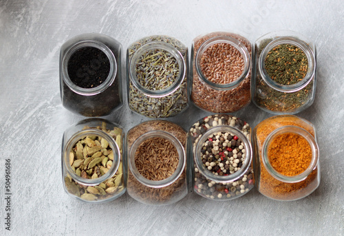 Different types of spices in glass jars. Close up photo of food flavors. Cardamom  turmeric  lavender  curry  pepper and flax seeds. 
