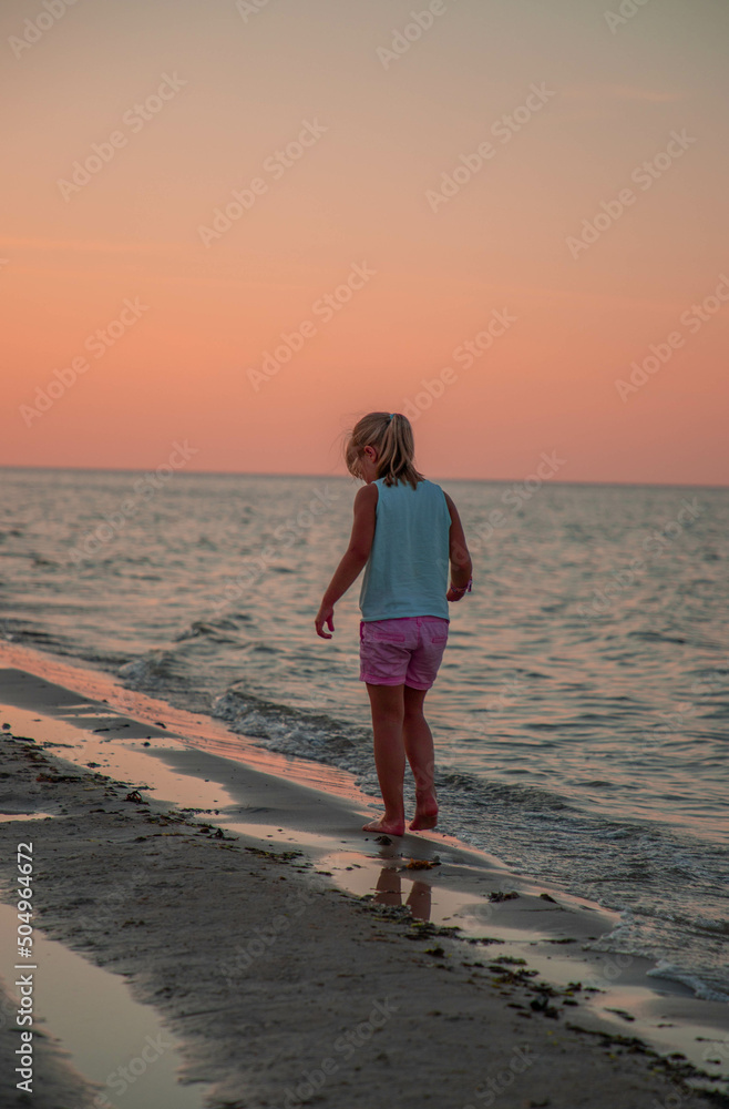 Girl in rose shorts walking alone on the beach in the summer sunset
