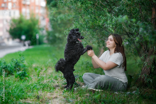 Charming plus size girl with long brown hair with a dog in a park in nature, a young woman and a pet black poodle