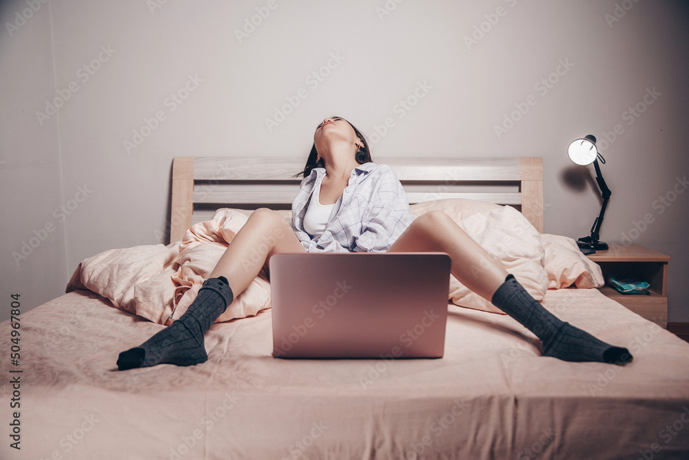 Foto Stock a young Asian webcam model girl is sitting in front of a laptop  with her legs spread. she communicates and shows her charms. low depth of  focus,artistic photo processing