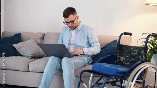 Smart employee working by using laptop that is on the table. Disabled man is in the wheelchair at home photo