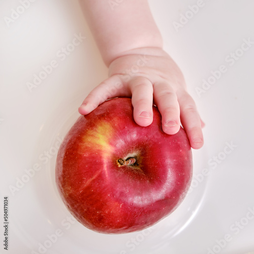 Baby hand and red apple fruit, close-up. Children fingers and an object on a white background