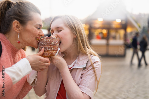 happy mother and daughter at fair in city eating trdelnik