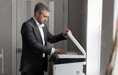 An adult successful man in a gray business suit stands near a copier