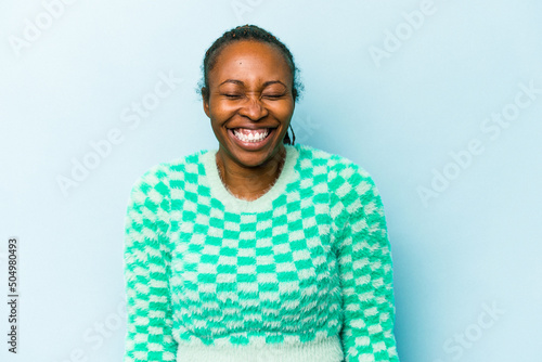 Young african american woman isolated on blue background laughs and closes eyes, feels relaxed and happy.