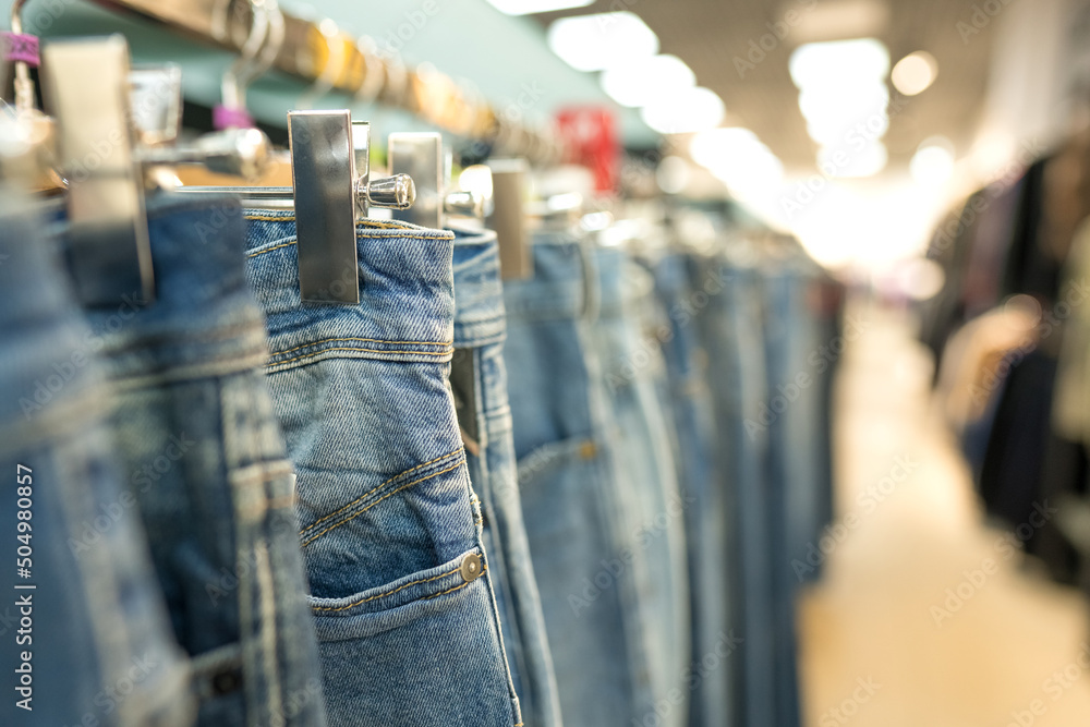Naklejka premium Jeans on hangers - new fashion collection at fashionable clothes store. Clothing rental or reselling concept. Clothes stall against blurred store background with copy space