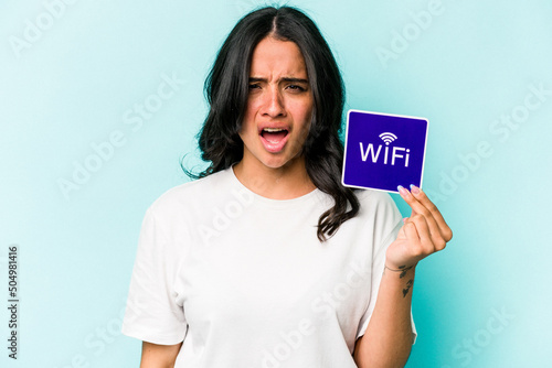 Young hispanic woman holding wifi placard isolated on yellow background screaming very angry and aggressive.