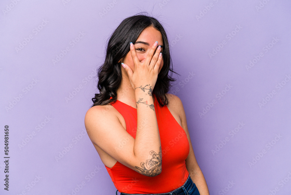 Young hispanic woman isolated on purple background blink at the camera through fingers, embarrassed covering face. Young hispanic woman isolated on purple background blink at the camera through fingers, embarrassed covering face.