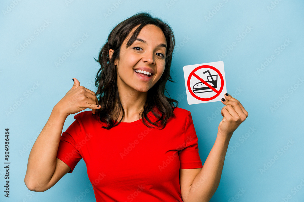 Young hispanic woman holding no eating sign isolated on blue background showing a mobile phone call gesture with fingers. Young hispanic woman holding no eating sign isolated on blue background showing a mobile phone call gesture with fingers.