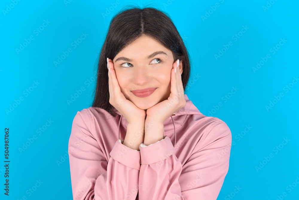 Inspired young beautiful Caucasian woman wearing pink raincoat over blue wall looking at copyspace having thoughts about future events Inspired young beautiful Caucasian woman wearing pink raincoat over blue wall looking at copyspace having thoughts about future events