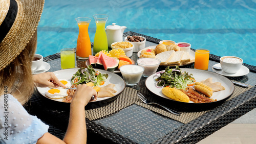Buffet service. Tasty breakfast served on table. Travel woman in hat eating breakfast is served with eggs, sausage, coffee, fresh orange juice, croissants, exotic fruits. Balanced diet on vacation © TravelMedia