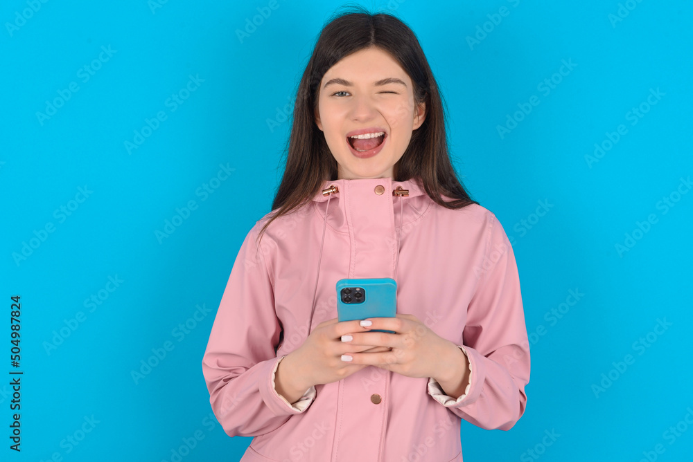 young beautiful Caucasian woman wearing pink raincoat over blue wall taking a selfie  celebrating success