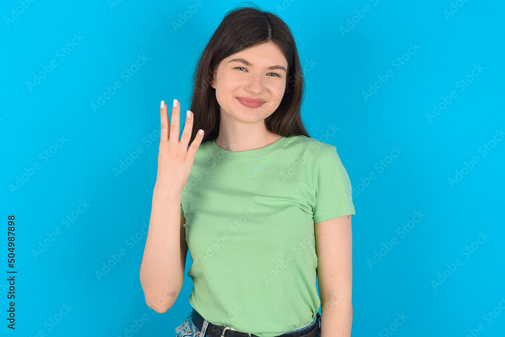 young beautiful Caucasian woman wearing green T-shirt over blue wall smiling and looking friendly, showing number four or fourth with hand forward, counting down young beautiful Caucasian woman wearing green T-shirt over blue wall smiling and looking friendly, showing number four or fourth with hand forward, counting down