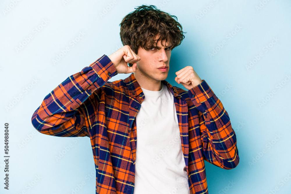 Young caucasian man isolated on blue background throwing a punch, anger, fighting due to an argument, boxing. Young caucasian man isolated on blue background throwing a punch, anger, fighting due to an argument, boxing.
