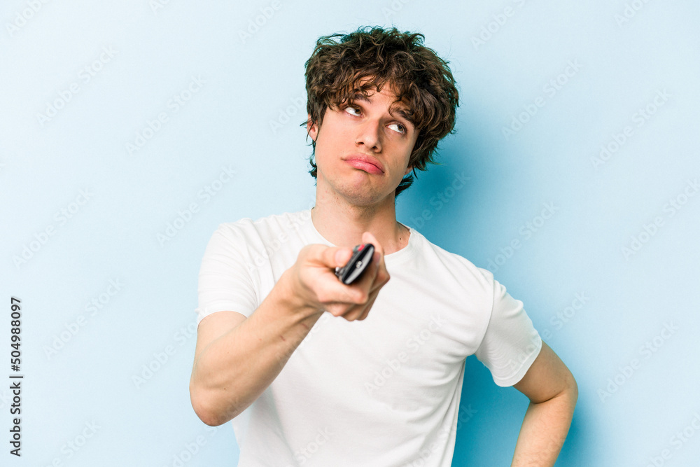 Young caucasian man holding tv controller isolated on blue background Young caucasian man holding tv controller isolated on blue background
