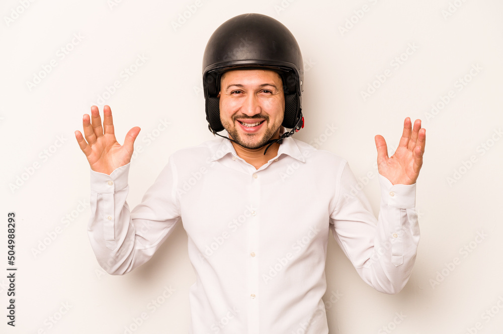 Hispanic business man going to work with motorcycle isolated on white background receiving a pleasant surprise, excited and raising hands. Hispanic business man going to work with motorcycle isolated on white background receiving a pleasant surprise, excited and raising hands.