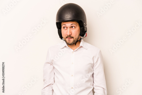 Hispanic business man going to work with motorcycle isolated on white background confused, feels doubtful and unsure. © Asier