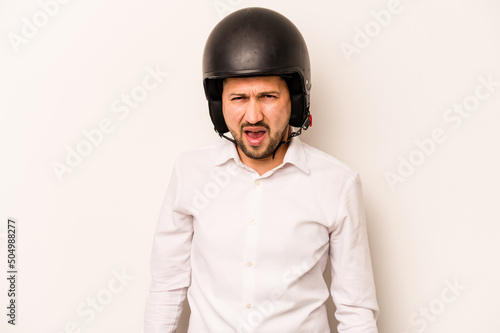 Hispanic business man going to work with motorcycle isolated on white background screaming very angry and aggressive.