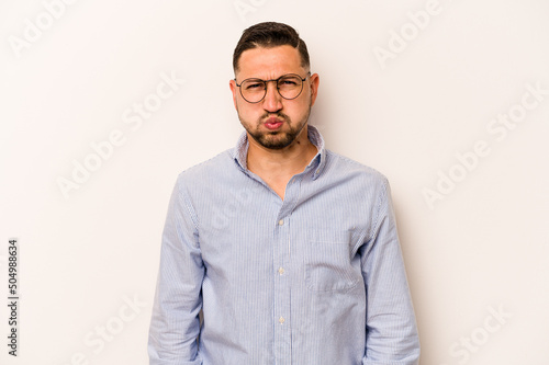 Young hispanic man isolated on white background blows cheeks, has tired expression. Facial expression concept. © Asier