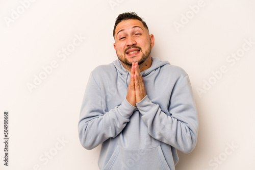 Young hispanic man isolated on white background holding hands in pray near mouth, feels confident. © Asier