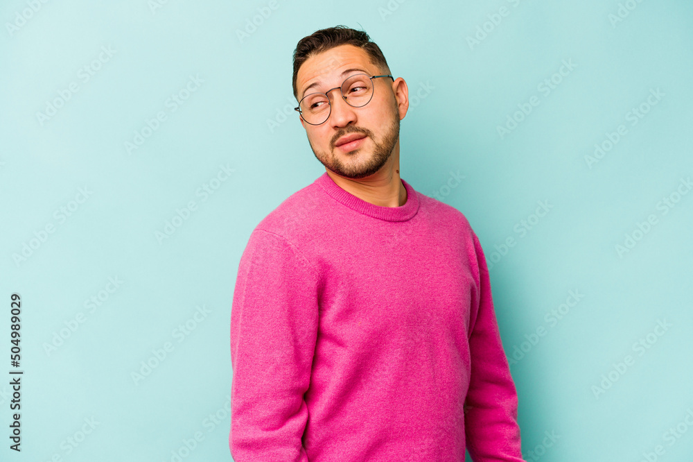 Young hispanic man isolated on blue background looks aside smiling, cheerful and pleasant. Young hispanic man isolated on blue background looks aside smiling, cheerful and pleasant.
