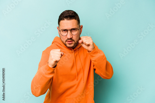 Young hispanic man isolated on blue background showing fist to camera, aggressive facial expression.